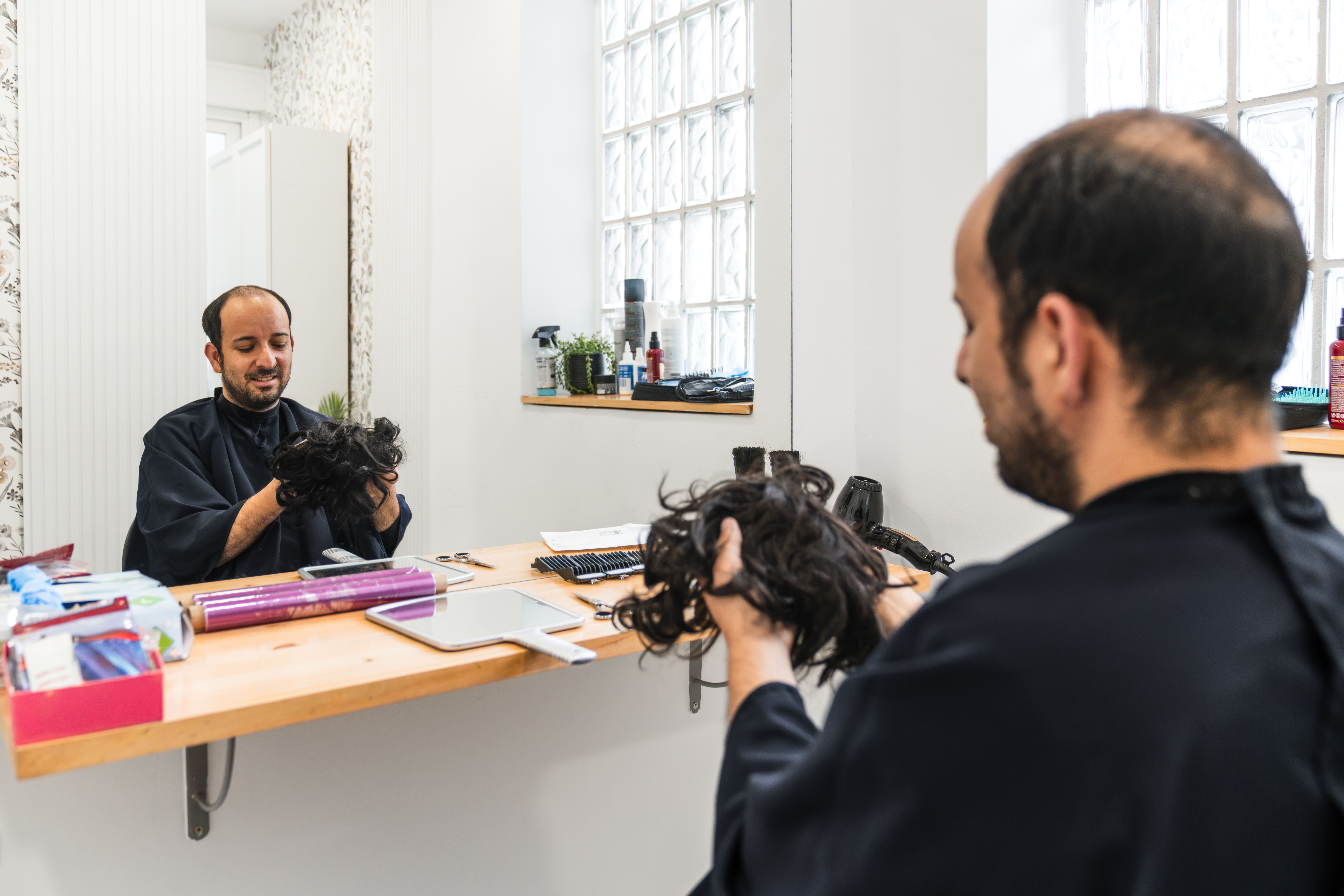 Man holding hair, looking in mirror.