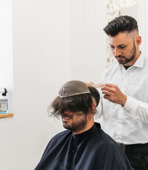 Barber fitting hairpiece on seated client.